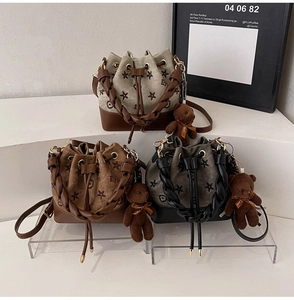 Detalle de bolsos tipo cubo bordados en beige, marrón y negro con colgantes de osito
