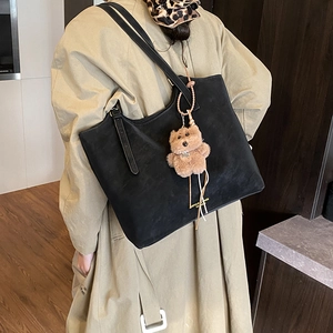Détail d'un grand sac cabas noir mat avec logo doré et charme d'ours en peluche