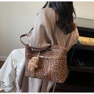 Lifestyle shot of large leopard print tote bag with plush bear charm and brown handles