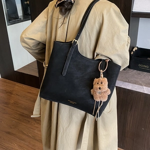 Détail du sac cabas en cuir noir mat avec boucle dorée et breloque ours en peluche