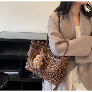 Detail of leopard print tote bag with brown leather straps and plush bear charm accent