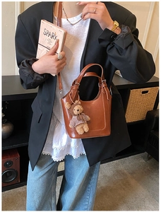 Close-up of brown leather bucket bag with a cute teddy bear charm and strap detail
