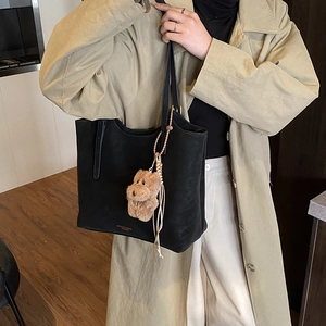Détail du grand sac cabas noir en cuir avec logo doré et pendentif ours sur un trench-coat
