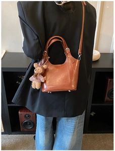 Close-up of brown faux leather bucket bag with cute teddy bear charm and adjustable strap