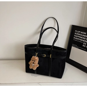 Detail of black suede tote bag with metal buckle strap and plush dog keychain
