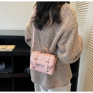 Detail of pink leather crossbody bag with gold buckles and reinforced corners on a model