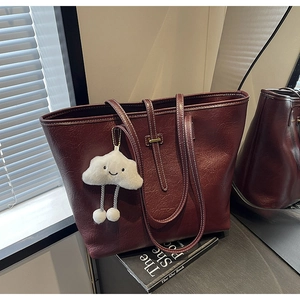 Close-up of burgundy tote bag with white contrast stitching and a cloud plush charm