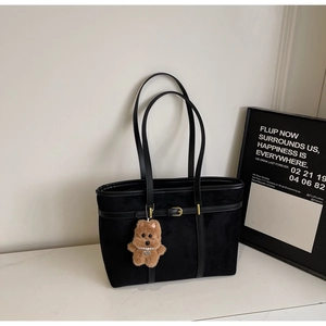 Detail of black suede tote bag featuring a leather strap buckle and a cute bear charm