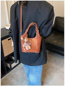 Detailed view of a brown bucket bag with plush bear charm and detachable strap