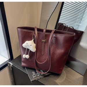 Close-up of burgundy PU leather tote bag with white stitching and plush cloud charm