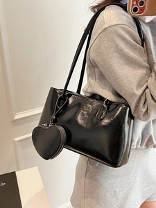 Glossy black oil wax leather tote bag with a heart-shaped purse charm on a model