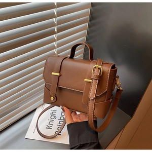 Detail of a brown vintage leather box bag with gold metal buckles and adjustable strap