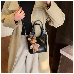 Detail of black glossy leather bucket bag featuring a teddy bear charm on khaki trench coat