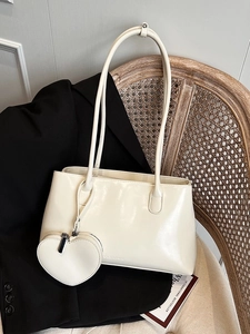 Cream oil wax leather tote bag with dual straps and heart pendant on a vintage chair