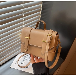 Detail of a minimalist khaki square bag with dual buckle design and gold hardware accents