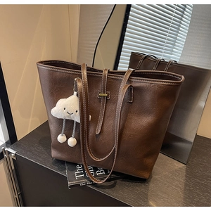 Detail of dark brown tote bag featuring contrast stitching and cloud plush charm
