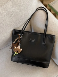 Retro black PU leather tote bag with white stitching and bear charm on a sofa