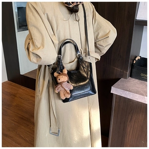 Detail of black glossy leather bucket bag with cute brown bear charm on khaki trench coat