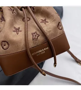 Detalle de bolso tipo cubo en lona bordada con base de cuero y cierre de cordón ajustable