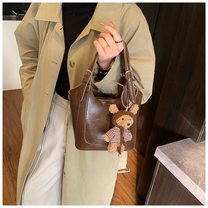 Brown bucket bag detail with adjustable handle and cute striped teddy bear charm accessory