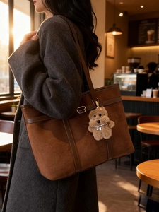 Brown suede tote bag with leather straps and a cute plush puppy pendant in a cafe setting