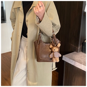 Detail of a dark brown vintage PU leather bucket bag with a cute bear charm and silver buckles