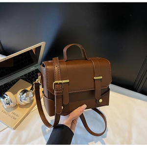 Detail of a dark brown vintage square bag with gold hardware and smooth leather finish