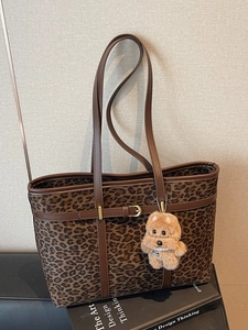 Large leopard print tote bag with brown leather handles and plush dog charm on black sofa