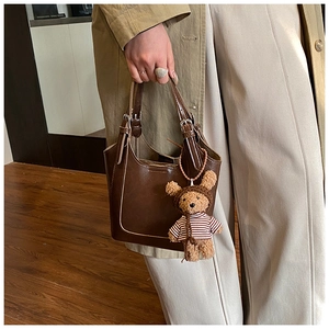 Detail of dark brown leather bucket bag with a cute plush bear pendant and metal buckles