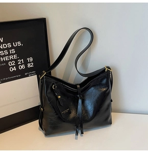 Detail of black faux leather tote with golden hardware, tassel and adjustable strap