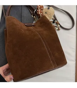 Detalle del bolso de ante marrón oscuro con costuras en contraste y colgante de osito