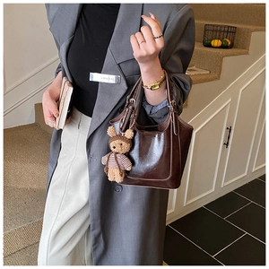 Detail of dark brown glossy bucket bag with cute bear charm and minimalist U-shaped design