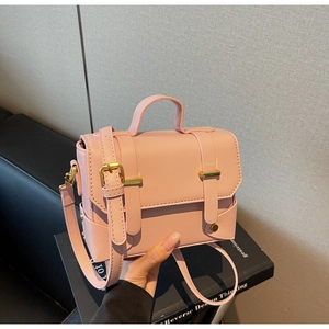 Pink rectangular crossbody bag with dual buckled straps and top handle in hand