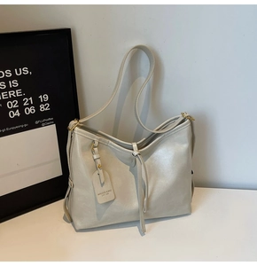 Close-up of cream PU leather tote bag with decorative strap and metallic brand tag