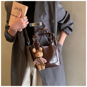 Detail of dark brown leather bucket bag with bear pendant held by a model