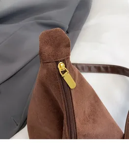 Close-up of golden hardware zipper on brown suede tote bag with textured shoulder strap