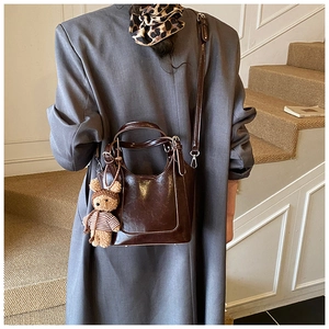 Detail of dark brown leather bucket bag with cute plush bear charm on grey suit