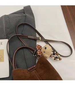 Detalle del bolso de ante marrón con un colgante de oso de peluche y correa ajustable