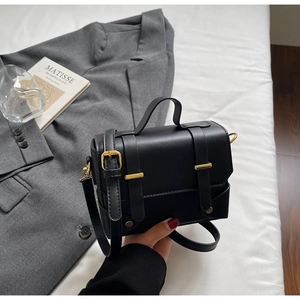 Chic black messenger bag with gold buckles and top handle on minimalist white bedding