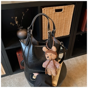 Detail of a shiny black bucket bag with a cute brown plush bear charm and metal buckle