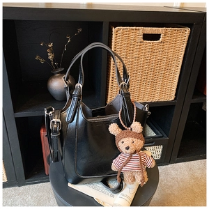 Detail of a black glossy bucket bag with silver zipper and a cute brown bear charm