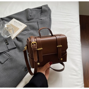 Close-up of brown leather square bag with vintage gold buckles and adjustable shoulder strap