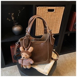Detailed view of brown leather bucket bag with cute bear charm on a vintage stool