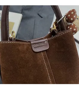 Detalle del bolso de cubo en ante marrón oscuro con anillo dorado y colgante de osito