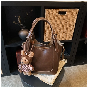 Close-up of a vintage dark brown leather bucket bag featuring a cute bear plush pendant