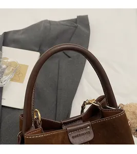 Detalle del bolso de ante marrón oscuro con costuras en contraste y asa de cuero