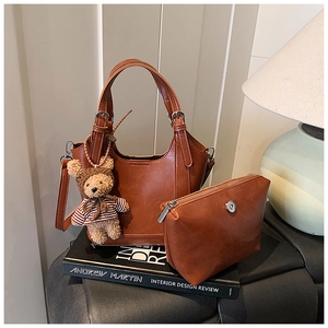 Brown leather bucket bag set with detachable strap and cute bear charm on a book