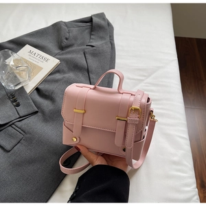 Detail shot of a pink square shoulder bag with gold buckles and adjustable strap