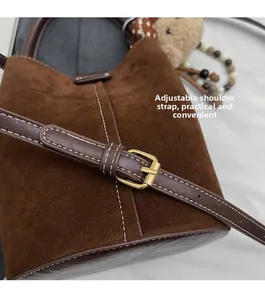 Detalle de la correa ajustable con hebilla dorada en el bolso tipo cubo de ante marrón