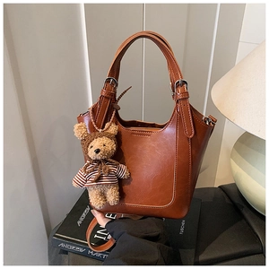 Close-up of brown faux leather bucket bag with teddy bear charm on a stack of books
